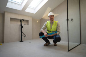 A man wearing a hard hat and safety vest kneels in a bathroom, inspecting or working on plumbing or fixtures during a bathroom remodeling project in San Francisco.