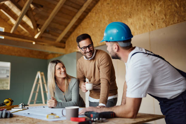 Happy couple discussing housing plans with a manual worker at a construction site—perfect example of complete home remodeling in Burlingame, CA.