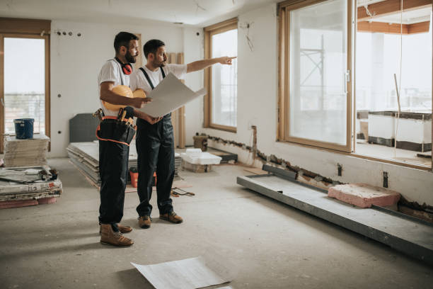 Full-length view of construction workers analyzing blueprints in an apartment while one aims into the distance—ideal for complete home remodeling in Burlingame, CA.