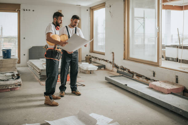 Two men examine construction plans for a whole home remodeling project in Tiburon, surrounded by building materials and tools.