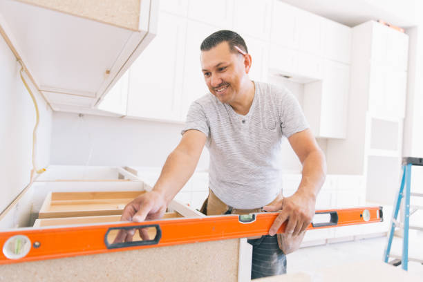 A man is focused on assembling a kitchen cabinet, surrounded by tools and materials in a well-lit workspace, part of a kitchen remodel in San Mateo.