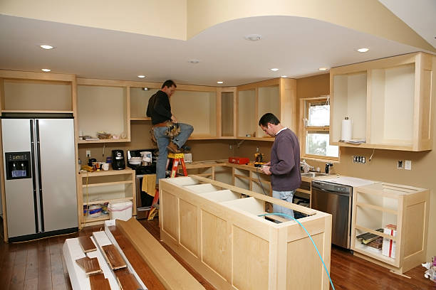 Cabinet maker installing custom-made kitchen island and cabinets, while electrician installs in-cabinet lighting during Burlingame kitchen remodeling.