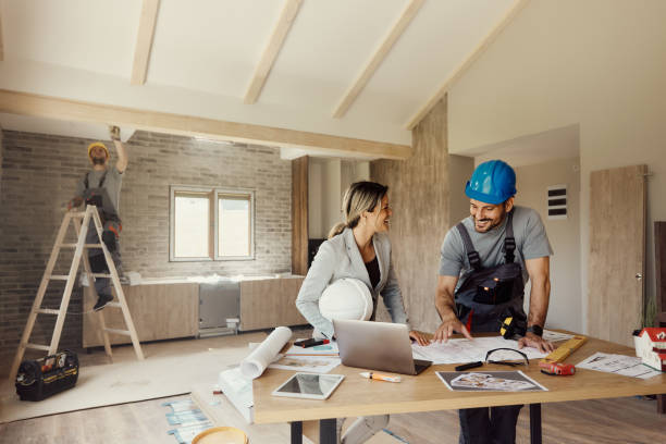 Happy female architect and manual worker communicating while analyzing blueprints at a Tiburon remodeling project. Copy space.