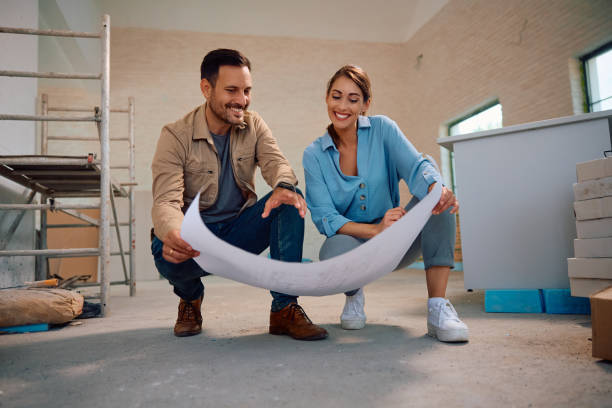 Happy female architect and manual worker communicating while analyzing blueprints at renovating house. Copy space.