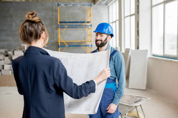 Foreman expertising the structure with businesswoman holding blueprints at the construction site indoors for the best remodeling company in San Francisco.