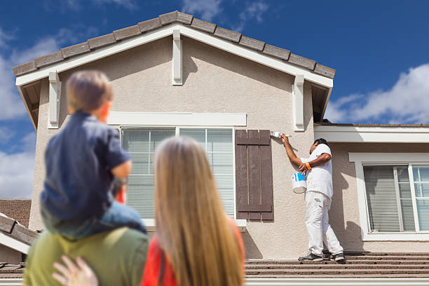 A man and woman are painting a house together during a complete home remodeling in Hillsborough, CA, while a child observes and enjoys the activity nearby.