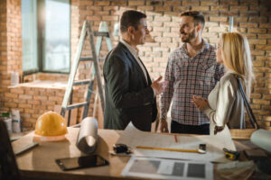 Three professionals discussing home remodeling plans in an office setting, surrounded by blueprints and design materials.