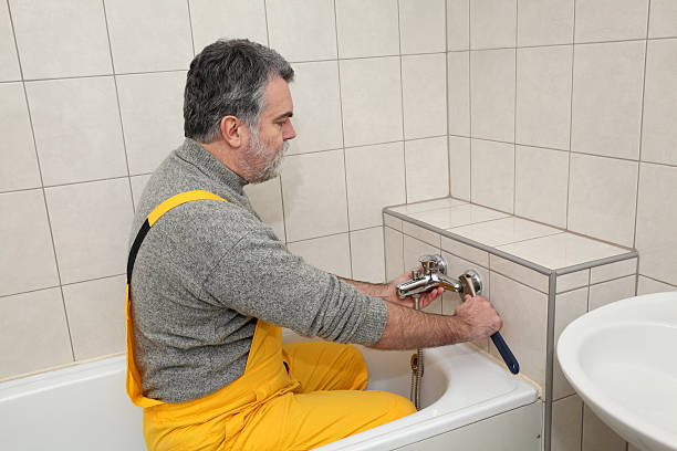 A plumber fixing a water tap at a bathtub in a bathroom, showcasing luxury bathroom remodeling in Hillsborough with expert craftsmanship.