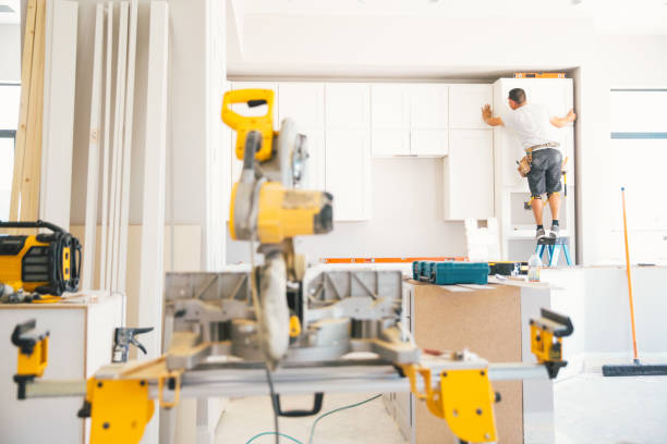 A man focused on assembling a kitchen cabinet, using tools and materials in a well-lit kitchen remodeling environment.